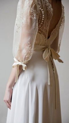 the back of a woman's wedding dress with lace and bows on her shoulders