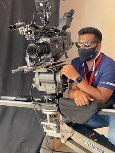 a man wearing a face mask sitting in front of a camera on a tripod