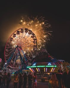 fireworks are lit up in the night sky above a ferris wheel at an amusement park