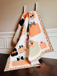 an orange and white cat quilt on top of a wooden floor next to a wall