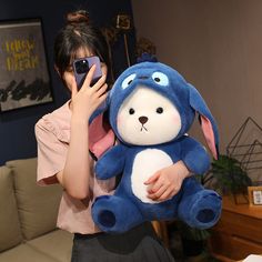 a woman holding a blue and white stuffed animal in her arms while looking at her cell phone