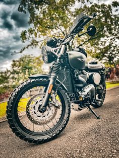 the motorcycle is parked on the side of the road in front of some trees and clouds