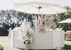 two vases with flowers and plants are under an umbrella on the grass near tables