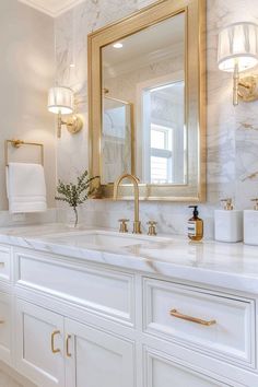 a white bathroom with gold accents and marble counter tops, along with large mirrors on the wall