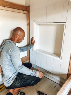 a man sitting on the floor in front of a cabinet with his hands up and pointing at it