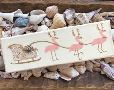 a wooden box filled with sea shells and pink flamingos painted on the front side