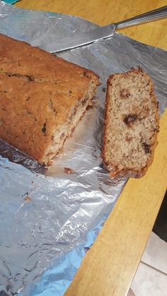 a loaf of bread sitting on top of aluminum foil next to a knife and fork