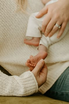 a woman holding a baby's hand while sitting on a couch in front of her