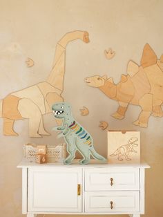 a toy dinosaur standing on top of a white dresser in front of a wall mural