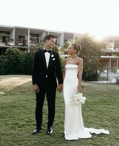 a man and woman in formal wear standing on the grass holding hands with each other