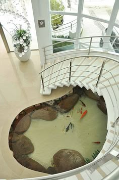 a fish pond in the middle of a spiral stair case that leads to an upper level balcony