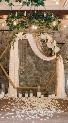 a stone wall with candles and flowers on it is decorated with greenery, white roses and hanging from the ceiling