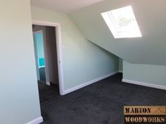 an empty room with a skylight and carpeted floor in the foreground, there is a door leading to another room