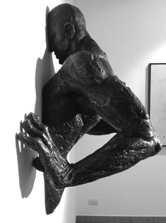 a black and white photo of a sculpture of a man leaning against a wall with his hands on his face