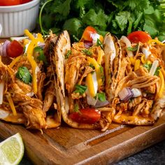 shredded chicken tacos on a cutting board with cilantro, limes and tomatoes