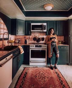 a woman standing in the middle of a kitchen with green cabinets and an area rug