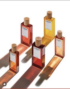 four bottles of perfume sitting on top of a white surface with long shadows behind them