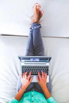 two people laying on a couch with their feet up and one person typing on a laptop