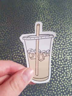 a hand holding up a sticker with an image of a drink and ice cubes in it