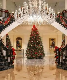 a christmas tree in the middle of a room with stairs and chandelier hanging from the ceiling