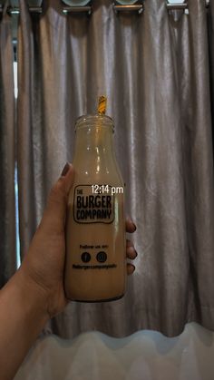 a person holding a jar of food in front of a curtain with the words burger company on it