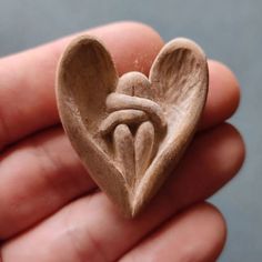 a hand holding a small wooden heart with two people in the shape of an angel