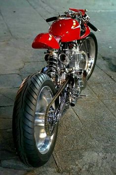 a red motorcycle parked on top of a cement road next to a sidewalk with no people