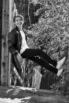 a young man is hanging off the side of a wooden fence with his feet in the air