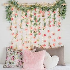 a bed topped with pillows covered in pink flowers and greenery next to a white wall