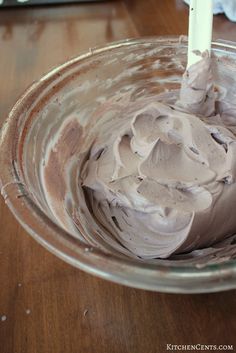 a mixing bowl filled with chocolate frosting on top of a wooden table