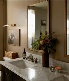 a bathroom sink sitting under a large mirror next to a vase with flowers on it