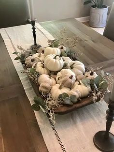 a wooden table topped with lots of white pumpkins and greenery on top of it