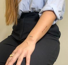 a woman with a small tattoo on her left arm, sitting in a black pants