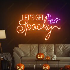 a living room filled with furniture and lots of pumpkins in front of a neon sign that says let's get spooky