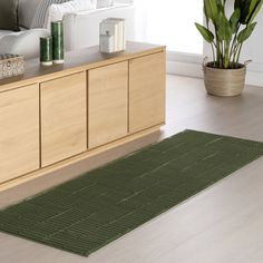 a living room with a green rug on the floor next to a wooden cabinet and potted plant