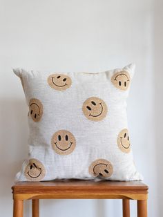 a pillow with smiley faces on it sitting on a wooden stool next to a white wall