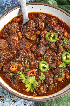 a bowl filled with meat and vegetables on top of a blue table cloth next to a spoon