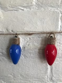 three christmas lights are hanging on a rope against a white brick wall, one red and one blue