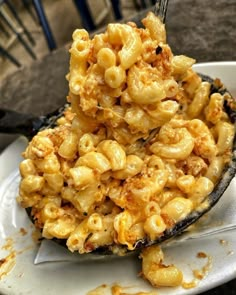 a spoon full of macaroni and cheese on top of a plate with a fork