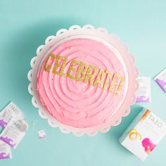 a pink cake with the word celebration spelled in gold letters on it next to other items