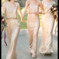 three bridesmaids walking down the street in gold gowns and holding hands with each other