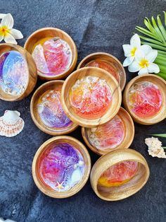 six wooden bowls filled with different colored liquids on top of a black surface next to flowers