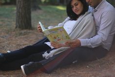 a man and woman sitting on the ground reading a book