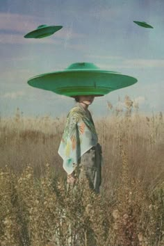 a woman standing in tall grass with two green hats on her head and one hat over her head