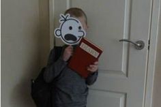 a young boy holding a book with a face cut out of it