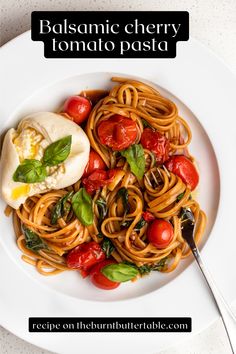 a white plate topped with pasta, tomatoes and spinach on top of a table