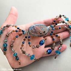 a woman's hand holding a beaded bracelet with blue and brown beads on it