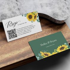 two sunflowers are on top of a wooden table with a green and white business card