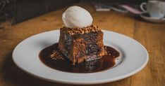 a piece of cake with ice cream on top sits on a plate in front of a cup