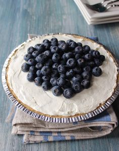 a pie with blueberries on it sitting on top of a table next to napkins